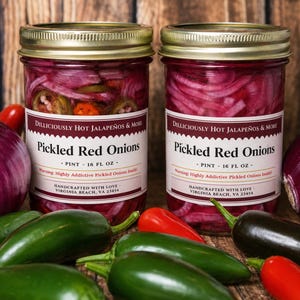Peut inclure: Deux bocaux en verre d'oignons rouges marinés aux piments jalapeños. Les bocaux ont des couvercles dorés et des étiquettes blanches indiquant "Pickled Red Onions" et "Dilliciously Hot Jalapeños & More". Les bocaux sont entourés de piments jalapeños frais, d'oignons rouges et de poivrons rouges.