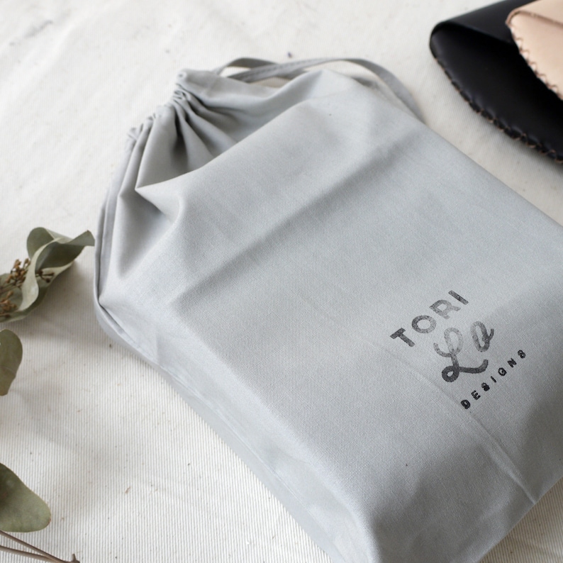 May include: A gray drawstring bag with the text "TORI Lee DESIGNS" printed on the front.