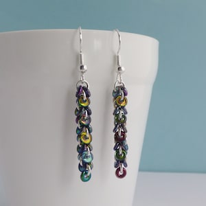 May include: A pair of silver dangle earrings with iridescent rainbow colored beads. The beads are round and have a metallic finish.