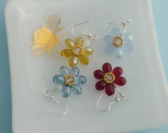 May include: Four flower-shaped earrings with silver-tone hooks. Each earring features six teardrop-shaped petals surrounding a gold-beaded center. The petals are translucent yellow, light blue, blue crackle, and deep red. A gold bee decal is visible.