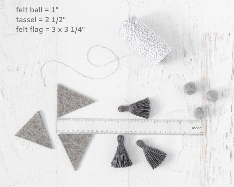May include: A close-up of craft supplies for making a felt garland. The supplies include felt balls, felt triangles, tassels, and twine. The felt balls are 1 inch in diameter, the tassels are 2 1/2 inches long, and the felt triangles are 3 inches by 3 1/4 inches. The image also includes a ruler and the text "oboot".