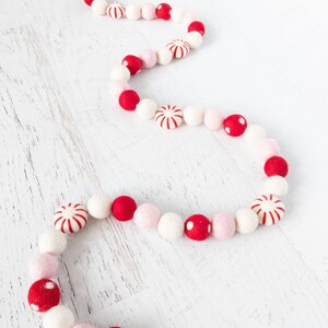 May include: A festive garland made of felt balls in red, white, and pink. The garland features alternating colors and candy cane designs.