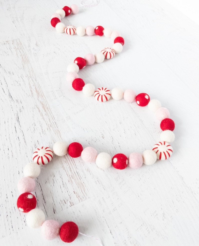 May include: A festive garland made of felt balls in red, white, and pink. The garland features alternating colors and candy cane designs.