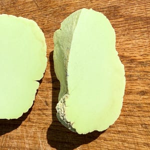 May include: Two pieces of light green polished stone, shaped like a heart, on a wooden surface.
