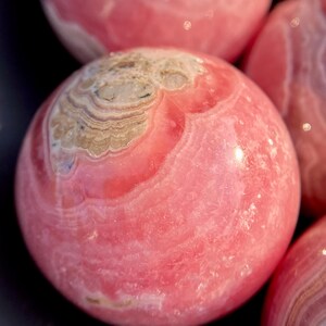 Może przedstawiać: Polished sphere of pink calcite, a type of mineral, with pink and white stripes.