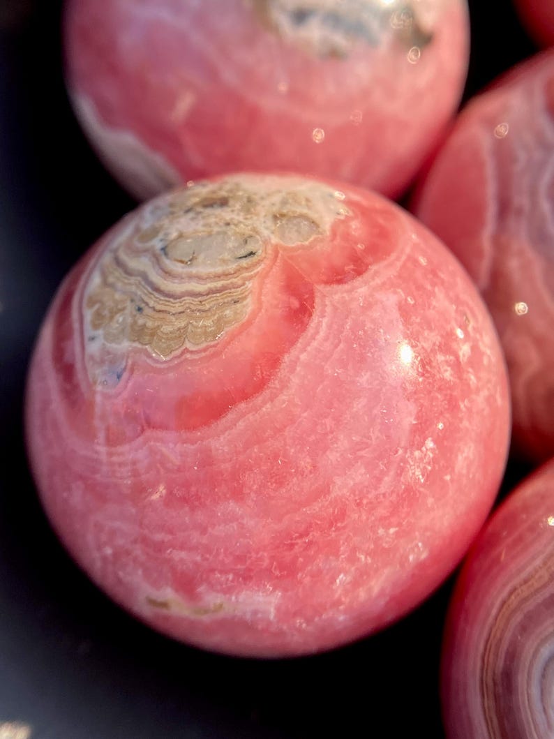 Może przedstawiać: Polished sphere of pink calcite, a type of mineral, with pink and white stripes.