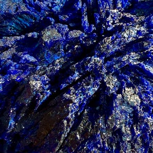 May include: Close-up of a deep blue mineral formation with crystalline structures. The surface reflects light, creating a shimmering effect. The mineral's color ranges from dark indigo to bright sapphire.