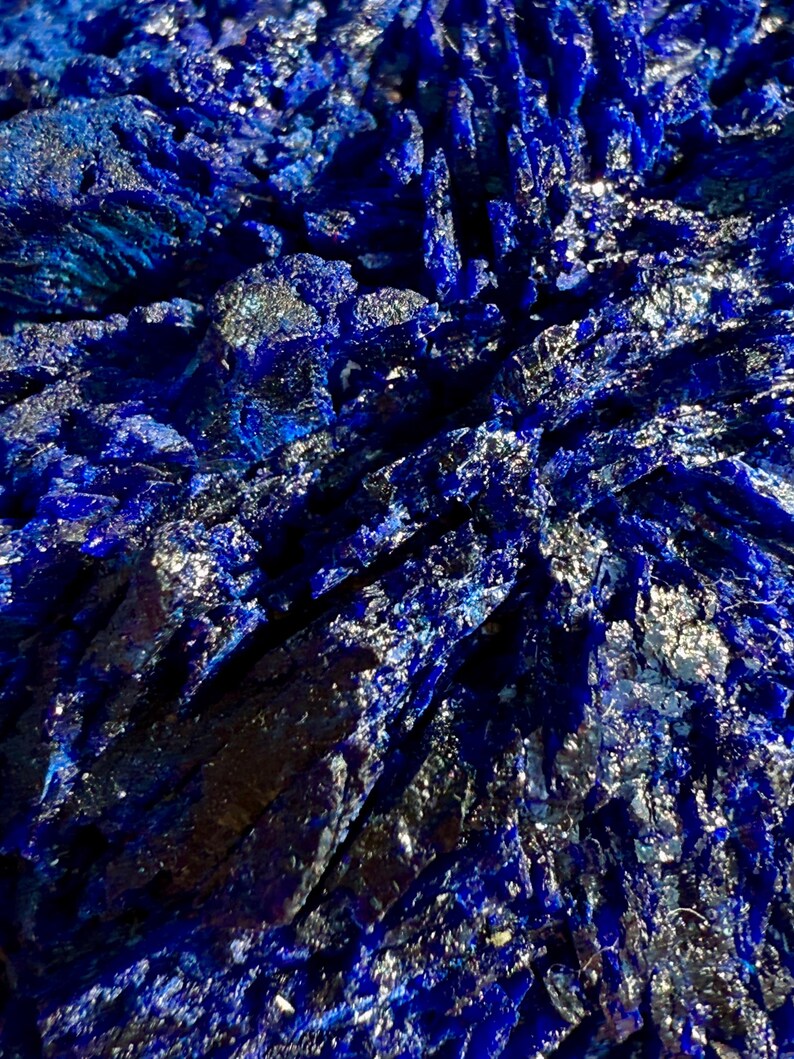 May include: Close-up of a deep blue mineral formation with crystalline structures. The surface reflects light, creating a shimmering effect. The mineral's color ranges from dark indigo to bright sapphire.
