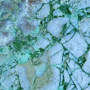 May include: Close-up of a light blue and green marble surface with a cracked and veined pattern.