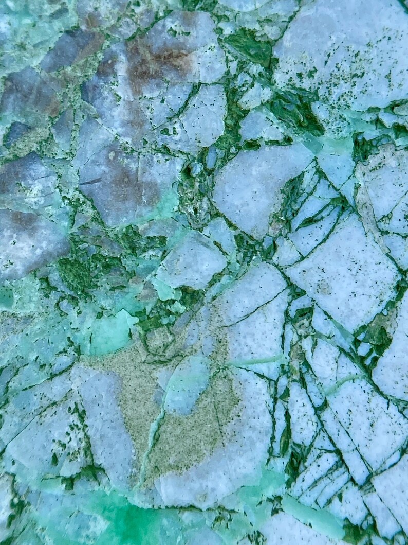 May include: Close-up of a light blue and green marble surface with a cracked and veined pattern.