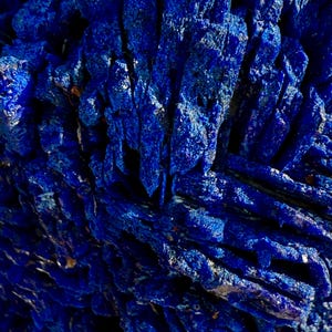 May include: Close-up of a deep blue mineral formation with a crystalline structure. The surface has a rough, textured appearance with sharp, angular formations. The color is a rich, saturated blue, with hints of lighter shades in the crevices.