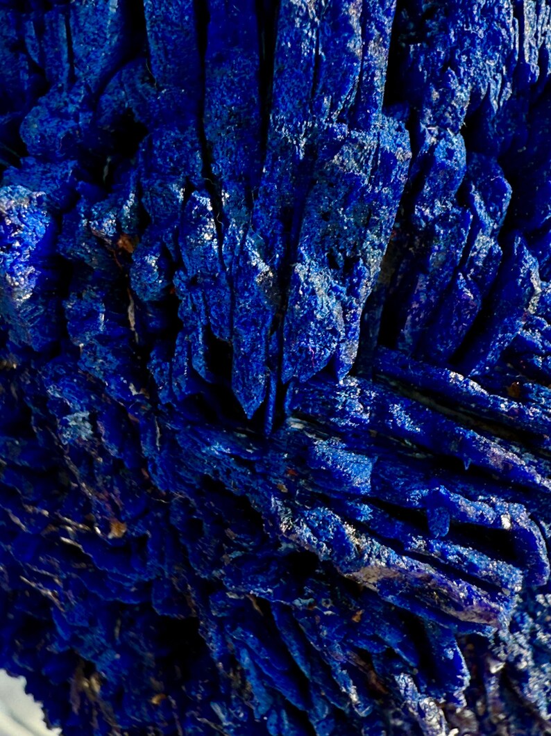 May include: Close-up of a deep blue mineral formation with a crystalline structure. The surface has a rough, textured appearance with sharp, angular formations. The color is a rich, saturated blue, with hints of lighter shades in the crevices.