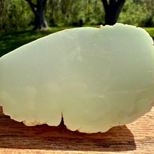 May include: A large, light green, irregularly shaped piece of polished jade. The jade has a smooth, polished surface and a rough, natural edge.
