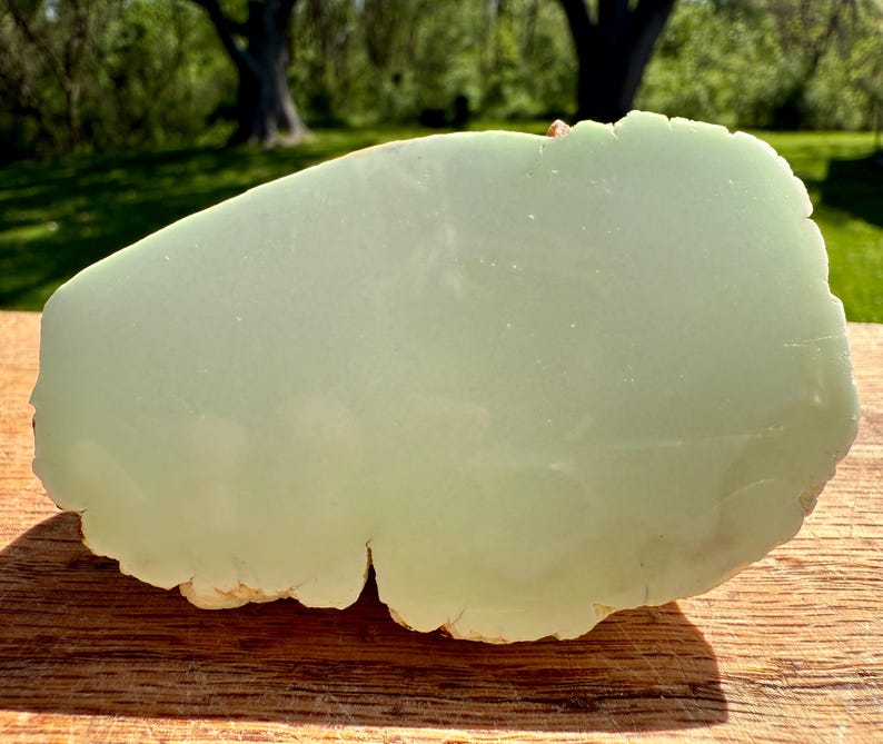 May include: A large, light green, irregularly shaped piece of polished jade. The jade has a smooth, polished surface and a rough, natural edge.