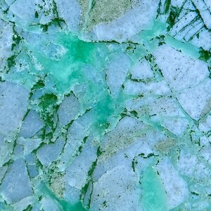 May include: Close-up of a green and white agate stone with a cracked and broken surface. The stone has a natural, organic look and feel.