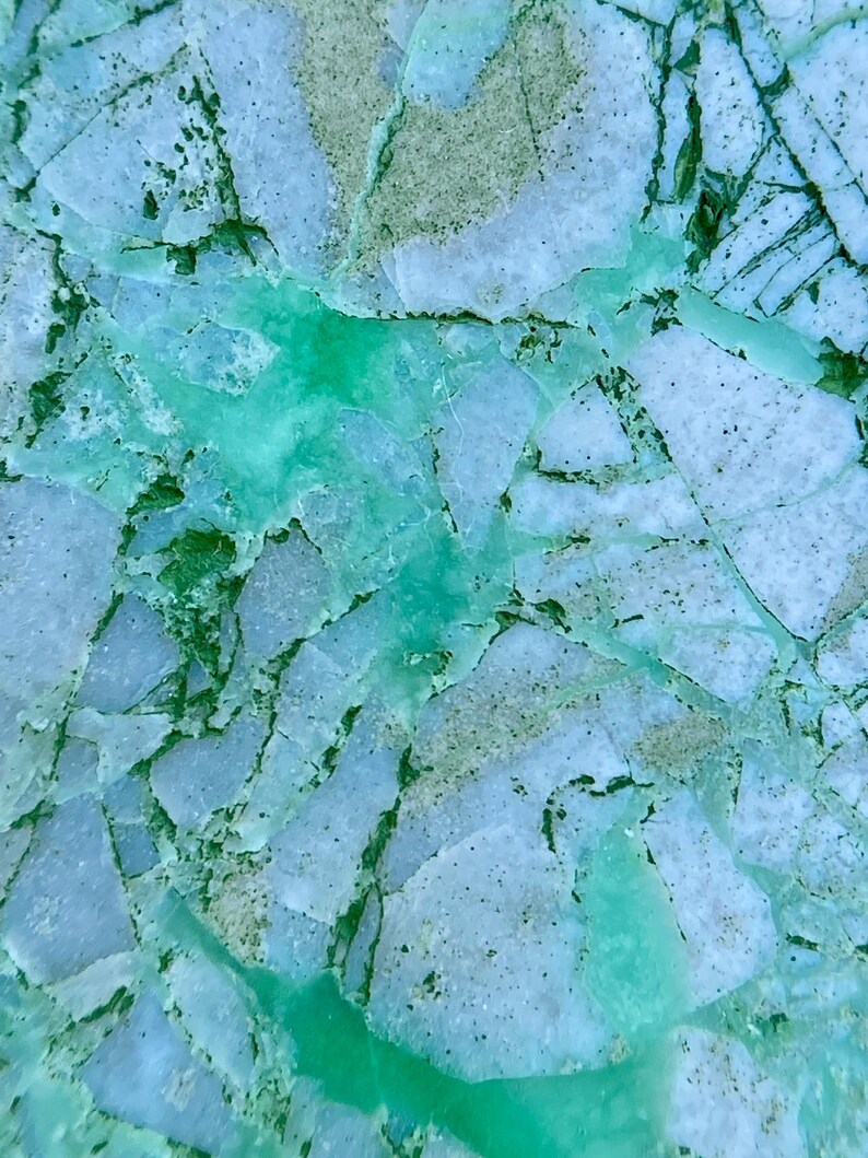 May include: Close-up of a green and white agate stone with a cracked and broken surface. The stone has a natural, organic look and feel.