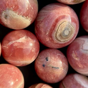 Może przedstawiać: Kolekcja gładkich, okrągłych, polerowanych kul z kamieni szlachetnych w kolorze r&oacute;żowym i białym. Kule mają naturalny, organiczny wygląd.