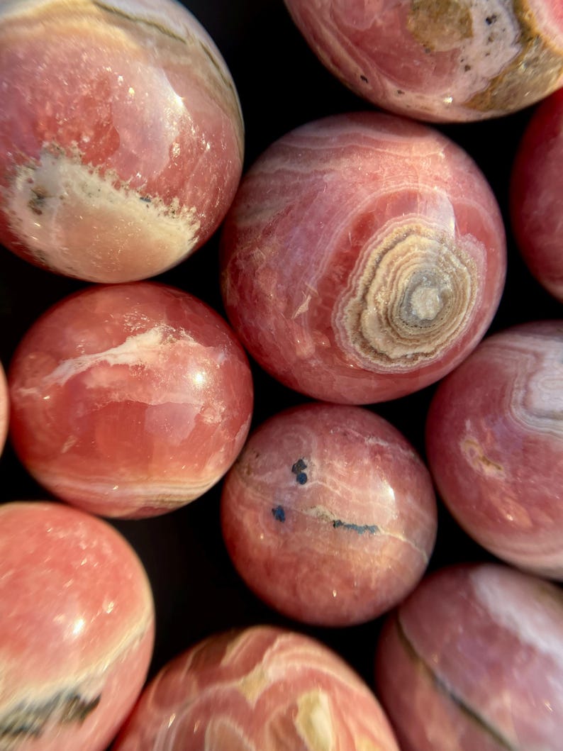 Może przedstawiać: Kolekcja gładkich, okrągłych, polerowanych kul z kamieni szlachetnych w kolorze r&oacute;żowym i białym. Kule mają naturalny, organiczny wygląd.