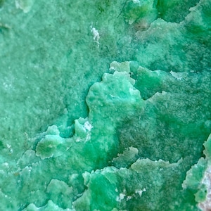 May include: Close-up of a green, textured stone with a rough surface. The stone has a mottled appearance with shades of light and dark green.