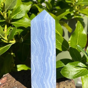 May include: A blue agate crystal point with a pointed top and a smooth, polished surface. The crystal has a banded pattern of light and dark blue.
