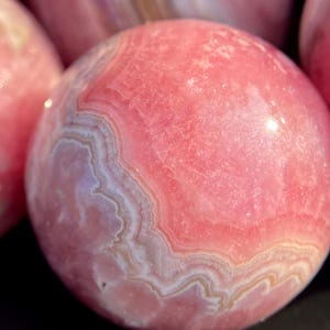 Może przedstawiać: Polished pink calcite sphere, a type of mineral, with pink and white bands.
