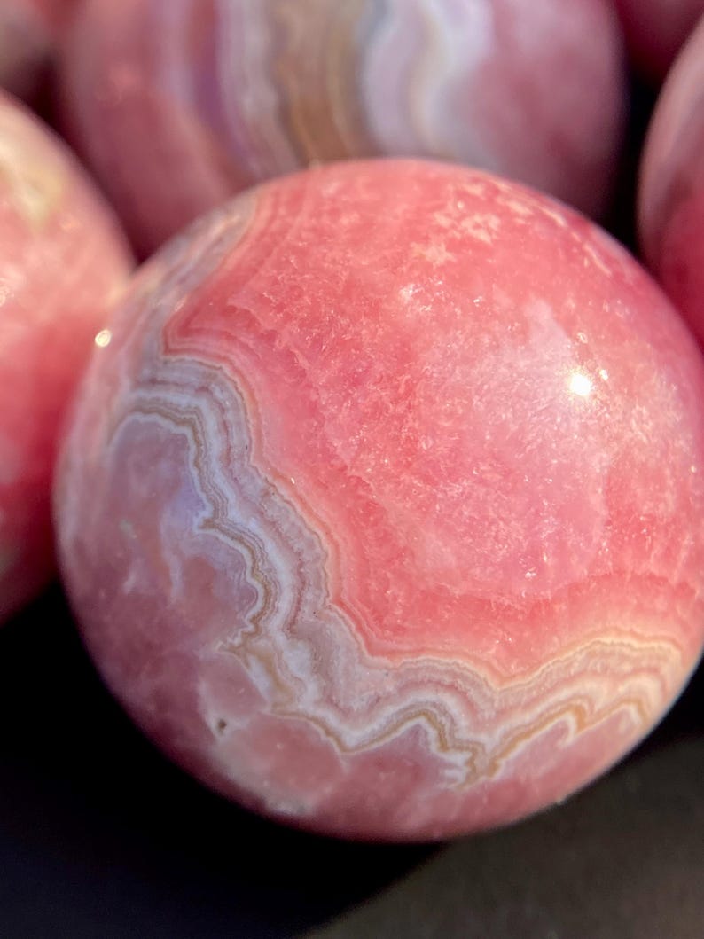 Może przedstawiać: Polished pink calcite sphere, a type of mineral, with pink and white bands.