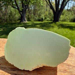 May include: A large, light green, smooth, polished, oval-shaped piece of green serpentine stone. The stone has a slightly rough, natural edge.