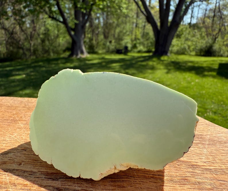 May include: A large, light green, smooth, polished, oval-shaped piece of green serpentine stone. The stone has a slightly rough, natural edge.