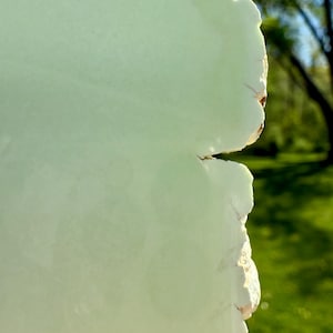 May include: A close-up of a light green, irregularly shaped, natural stone with a rough, textured edge.