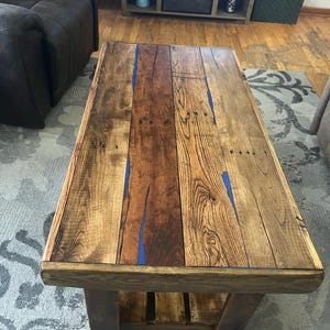 May include: A rustic wooden coffee table with a blue epoxy inlay. The table has a lower shelf and is made of reclaimed wood.