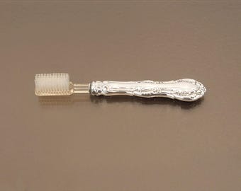 May include: A silver toothbrush with a decorative handle and white bristles.