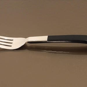 May include: A silver fork with a black plastic handle. The fork has four tines and is lying on a brown surface.