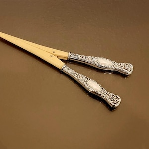 May include: A pair of antique silver letter openers with ivory handles. The handles are decorated with intricate floral patterns.
