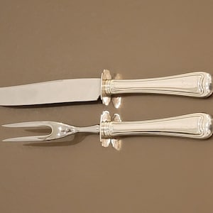 May include: A silver carving set with a knife and fork. The handles are ornate and have a polished finish.