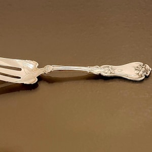 May include: A silver fork with an ornate handle. The fork has three tines and a decorative design on the handle.