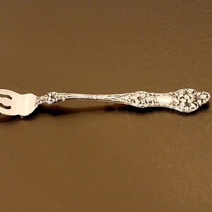 May include: A silver fork with an ornate design. The fork has three tines and a long handle.