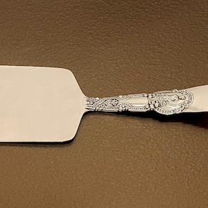 May include: A silver cake server with an ornate handle. The blade is rectangular and the handle is decorated with a floral design.