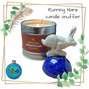 May include: A white ceramic hare candle snuffer with a blue base. The snuffer is sitting on top of a tin candle labeled "Purbeck Candles Spiced Orange".