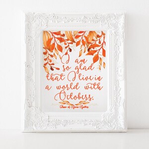 May include: A white framed print with a watercolour illustration of autumn leaves in shades of orange and gold. The print features the quote "I am so glad that I live in a world with Octobers." by the author "Her of Gsus Gubles".