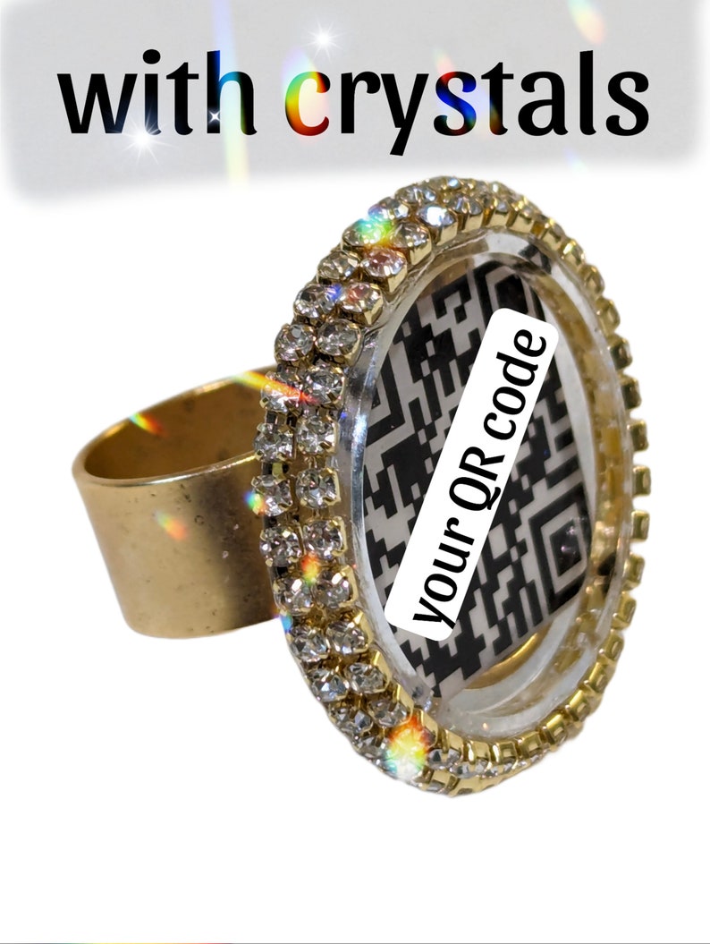 May include: A gold ring with a clear round bezel set with rhinestones. The bezel contains a black and white QR code with the text "your QR code" printed on it.