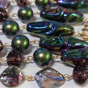 Pu&ograve; includere: Una collana multifilo con perline iridescenti in tonalit&agrave; di viola, verde e oro. Le perline sono di varie forme, tra cui rotonda, ovale e a goccia.