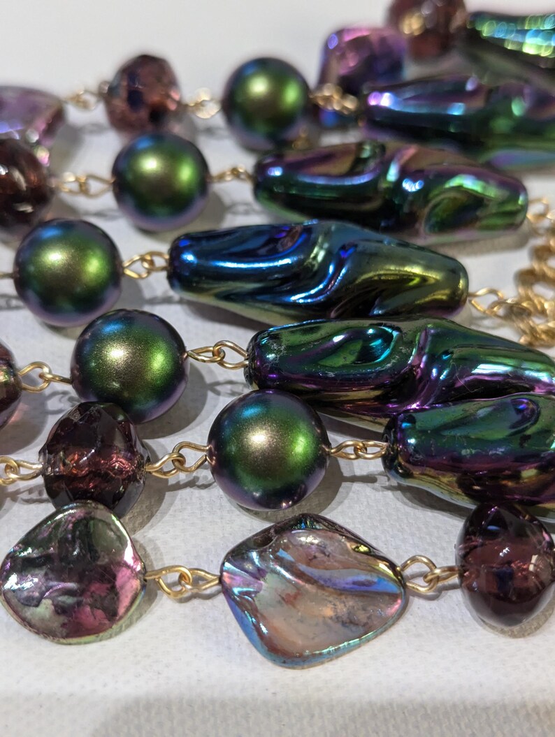 Pu&ograve; includere: Una collana multifilo con perline iridescenti in tonalit&agrave; di viola, verde e oro. Le perline sono di varie forme, tra cui rotonda, ovale e a goccia.