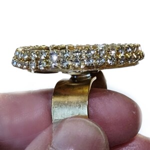 May include: A gold ring with a large, round, clear rhinestone setting. The ring is adjustable and has a simple band.