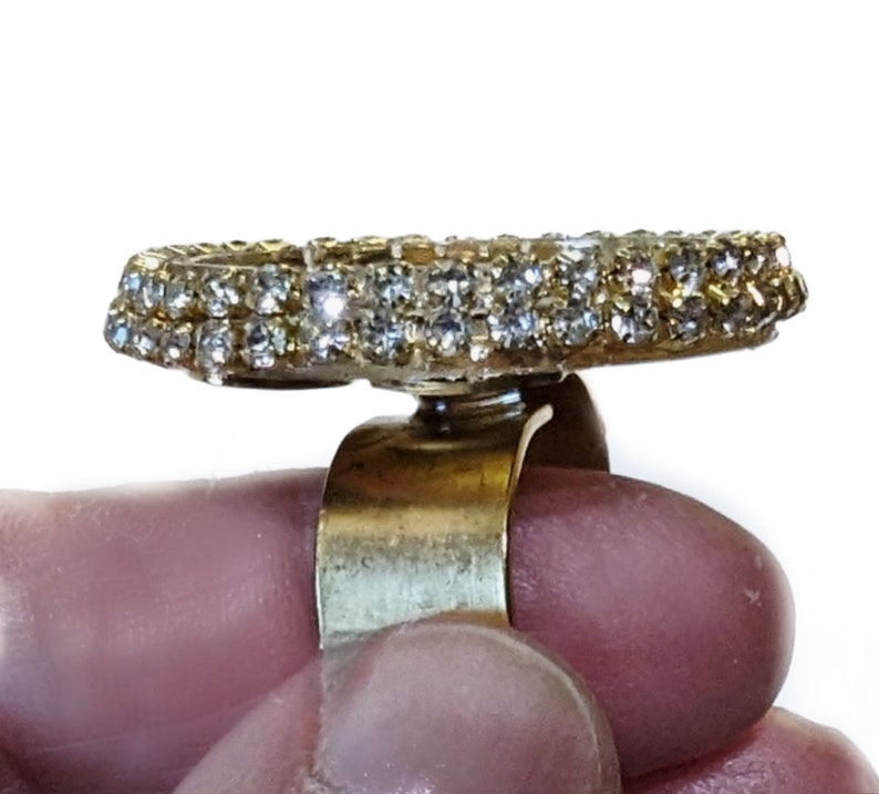 May include: A gold ring with a large, round, clear rhinestone setting. The ring is adjustable and has a simple band.