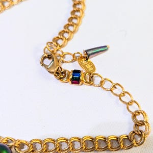 Pu&ograve; includere: Collana con catena dorata con una perla verde iridescente e un piccolo ciondolo con pietre multicolori. Il ciondolo ha il testo "J. Haller" su di esso.