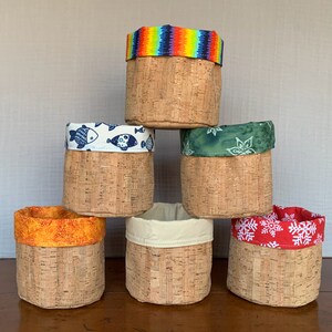 May include: Six cork-lined storage containers with fabric tops. The containers are stacked in a pyramid shape. The fabric tops feature different patterns, including fish, snowflakes, and a rainbow.