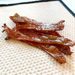 May include: Four strips of crispy, cooked bacon on a white, textured kitchen towel.
