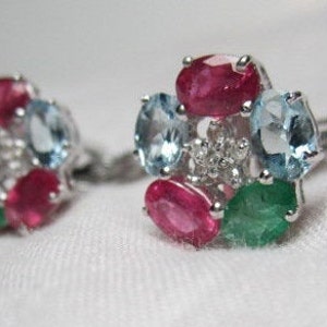 May include: A pair of silver earrings with a cluster of colorful gemstones. The earrings feature red, green, and blue gemstones set in a silver setting.