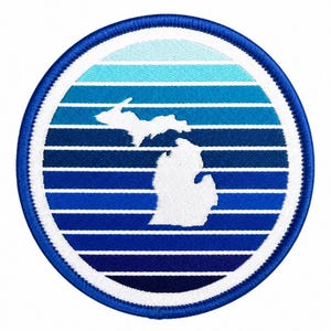 May include: A round patch featuring a white outline of the state of Michigan, set against a backdrop of horizontal blue stripes. The patch has a blue border and a white inner ring. The design evokes a retro, vintage aesthetic.