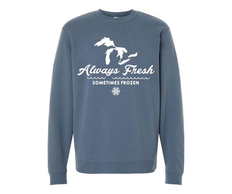 May include: A blue sweatshirt with the text "Always Fresh Sometimes Frozen" in white script, along with a white graphic of the Great Lakes and a snowflake. The sweatshirt is a solid color.
